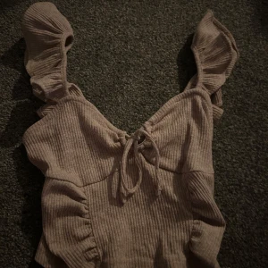 Beige ribbad topp med volangdetaljer - Säljer en beige ribbad topp med volangdetaljer på axelbanden och knytning framtill. Perfekt för en stilren och trendig look.