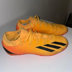 Fotbollsskor från Adidas - Snygga gula fotbollsskor från Adidas med svarta detaljer och snörning. Skorna har en modern design med en lätt och flexibel syntetisk ovandel, perfekt för snabba rörelser på planen. Använda ett par få gånger.