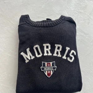 Morris tröja  - Säljer en blå tröja från Morris med vit text och ett emblem på framsidan. Tröjan har en rund halsringning och är perfekt för en avslappnad stil. Passar bra till jeans eller chinos.