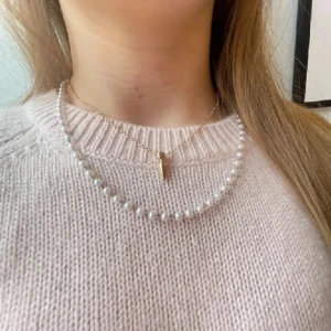 Halsband med pärlor och gulddetalj - Elegant halsband med vita pärlor och en guldfärgad detalj i mitten. Perfekt för att ge en klassisk touch till din outfit. Passar bra till både vardag och speciella tillfällen.