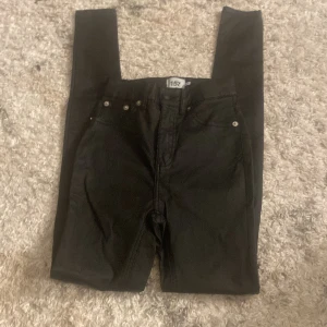 Svarta jeansbyxor från 157 - Snygga svarta jeansbyxor från 157 med klassisk femficksdesign och silverfärgade nitar. Perfekta för en stilren look. De har en dragkedja och knapp framtill. Lite slitna på knän