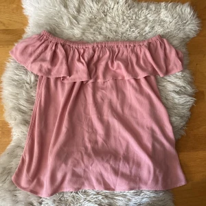 Rosa off-shoulder topp från ICHI - Säljer en superfin rosa off-shoulder topp från ICHI. Den är perfekt för sommaren med sin luftiga och bekväma passform. Toppen har en volangdetalj runt axlarna som ger en söt touch. Materialet känns mjukt och skönt mot huden. Perfekt för både vardag och fest!