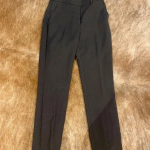 Svarta kostymbyxor - Säljer ett par stilrena svarta kostymbyxor. De är högmidjade och har en klassisk rak passform. Perfekta för både kontoret och finare tillfällen. Byxorna har hällor för bälte och en diskret dragkedja framtill.