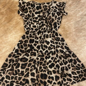 Leopardmönstrad klänning - Säljer en supercool leopardmönstrad klänning med volanger på ärmarna. Den är kort och perfekt för en festlig kväll. Klänningen har en elastisk midja som ger en fin passform och är tillverkad i ett mjukt och bekvämt material.