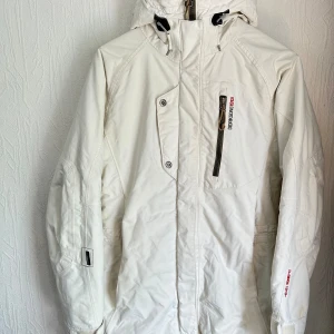 Didriksons1913 Vit jacka - Vit jacka med huva och dragkedja framtill. Jackan har två fickor framtill och en innerficka. Jackan har även en dragkedja i sidan. En bra och fin jacka med kvalite som är en perfekt vinterjacka / skidjacka. I bra skick. Kan inte se några hål.