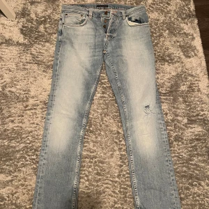 Ljusblå jeans med slitningar - Säljer ett par ljusblå jeans med slitningar på ena benet. De har en knappgylf och klassiska fem fickor. Jeansen är i bra skick och har en snygg tvätt som ger dem en cool look. Perfekta för vardagsbruk!                                                                     Hör av er i DM om ni har några frågor🙌