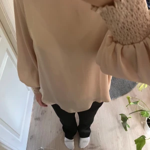 Beige blus med smockdetaljer - Säljer en superfin beige blus med långa ärmar och smockdetaljer vid ärmsluten. Perfekt för både vardag och fest! Den har en lös passform som gör den bekväm att bära hela dagen.