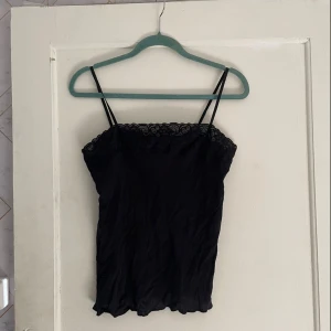 Svart linne från Calida - Säljer ett svart linne från Calida i storlek M. Det är ärmlöst med smala axelband och har en fin spetsdetalj längs kanten. Perfekt för både vardag och fest!