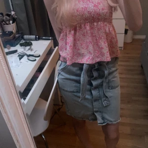 Jeanskjol med knappar och knytband - Säljer en superfin jeanskjol i ljus tvätt med knappar framtill och ett snyggt knytband i midjan. Kjolen har en klassisk design med fickor och är perfekt för både vardag och fest. Den är i mycket bra skick och nästan aldrig använd! den har högmidja