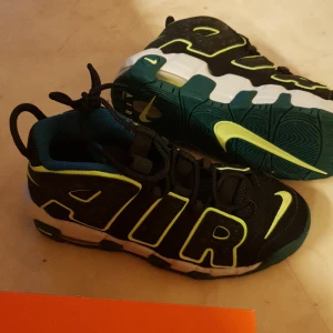 Svarta och gröna Nike sneakers - Säljer ett par coola Nike sneakers i svart och grönt. Skorna har en fet design med stora 'AIR' bokstäver på sidan och en grön Nike swoosh. De är perfekta för att sticka ut och har en bekväm passform med snörning. Sulan är vit med gröna detaljer, vilket ger en snygg kontrast. Nya var för små för sonen. 