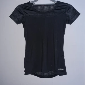 Svart kortärmad topp från Newbody - Säljer en svart kortärmad topp från Newbody. Den är perfekt för träning med sitt andningsbara material och diskreta mönster. Toppen har en tight passform och är i nyskick.