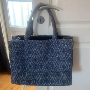 Mönstrad handväska från Maje - Säljer en snygg handväska från Maje med ett coolt mönster i denim. Väskan är rymlig och perfekt för vardagsbruk, får plats med dator. Väskan är i bra skick, köpt på Vestiaire Collective. Kan tänka mig att sälja för 1000 kr vid snabb affär.