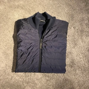 J.Lindeberg cardigan  - Säljer en J.Lindeberg hybrid cardigan i marinblå. Jackan är i väldigt bra skick, bara använd fåtal gånger. Det är storlek S. Köpte jackan för 3000kr, säljer den för 1590kr. Perfekt jacka till hösten. Har du några frågor är det bara att höra av dig! 