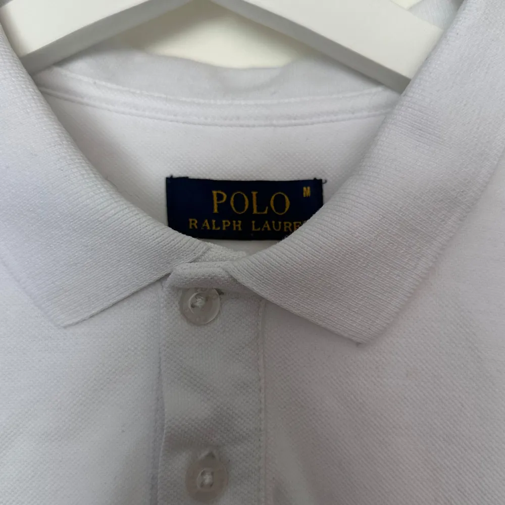 Säljer en klassisk vit pikétröja från Ralph Lauren. Den har korta ärmar och en stilren krage med tre knappar. Tröjan är i bomull och har den ikoniska broderade loggan på bröstet. Perfekt för en avslappnad men ändå stilren look!skick 7,5/10 vikitg inf. T-shirts.