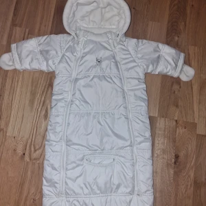 Åkpåse baby - Åkpåse med avtagbar luva och inbyggda handskar, 2 små fläckar nedtill vid dragkedjan, samt 1 liten fläck på flärpen som inte syns då det är på insidan, samt missfärgning innanför dragkedjan som inte syns när åkpåsen är stängd. Ej provat tvätta! 