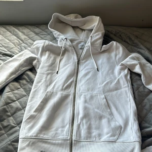Jack&jones vitt zip hoodie - Säljer min vita jack&jones hoodie då den inte passar längre, storlek S, skicket är väldigt bra den är ganska tjock i material dok har denna hoodie har en svart fläck av målar färg nere vid remmen
