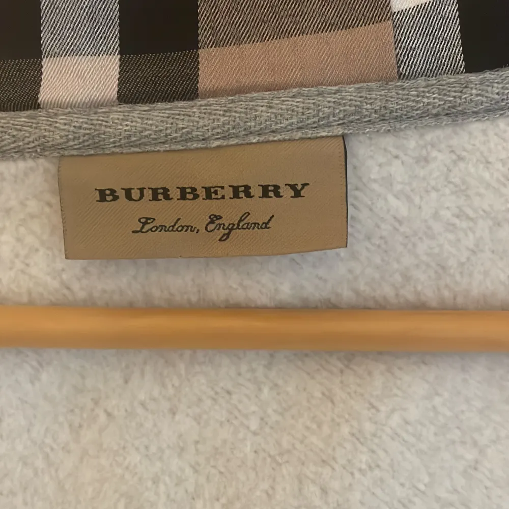 Säljer en snygg och stilren grå hoodie från Burberry. Den har en dragkedja framtill och en klassisk huva med det ikoniska Burberry mönstret på insidan. Perfekt för både vardag och lite finare tillfällen. Den är perfekt skick och superbekväm att ha på. Tröjor & Koftor.