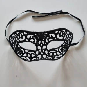 Svart spetsmask - Säljer en elegant svart mask. Perfekt för maskerad eller fest! Masken har ett vackert mönster och knyts enkelt med band bakom huvudet.