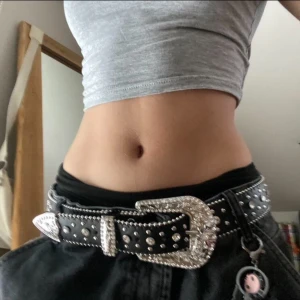 Svart bälte med silverdetaljer - Säljer ett snyggt svart bälte med massor av bling! Det har stora silverdetaljer och nitar, plus ett coolt kors på sidan. Perfekt för att ge din outfit lite extra edge. Passar bra till både jeans och kjol. 🤍😊