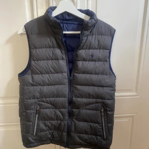 Ralph Lauren dubbel sidig väst - Mycket stilren Ralph väst. Västen har använt men har mycket kvar att ge och den är i ett 9/10 skick. Den enda defekter är att dragkedjan har behövts bytats vilket man kan se på bilderna. Nypris på västen är 2000kr, säljs för bra pris iom den e sälsyn