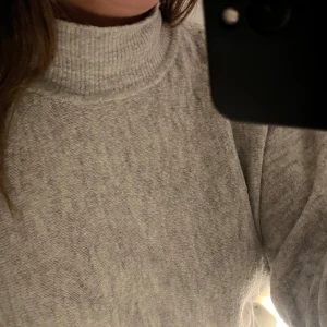 Grå stickad polotröja - Mysig grå stickad polotröja.Tröjan har en hög krage och långa ärmar. Lite längre baktill. Perfekt för höst/vinter. 
