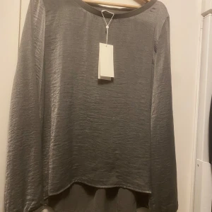 Grå långärmad topp från Vila - Säljer en stilren grå långärmad topp från Vila. Perfekt för en avslappnad look med sin enkla design och mjuka material. Toppen har en rund halsringning och är i storlek XL.