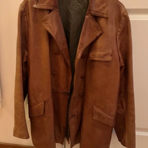 Brun skinnjacka vintage  - Säljer en snygg brun skinnjacka med klassisk krage och knappar framtill. Jackan har två stora fickor och en bröstficka, vilket ger en cool och avslappnad look. Perfekt för höst och vår! Jag är 171, size medium/ large beroende på! 