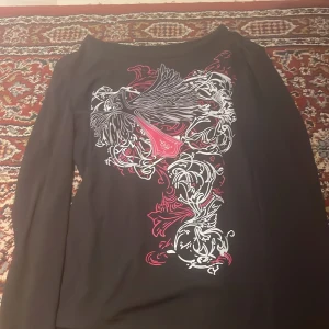 Svart långärmad topp med mönster - Snygg svart långärmad topp med ett detaljerat vitt och rött mönster framtill. Perfekt för att ge din outfit en unik touch.