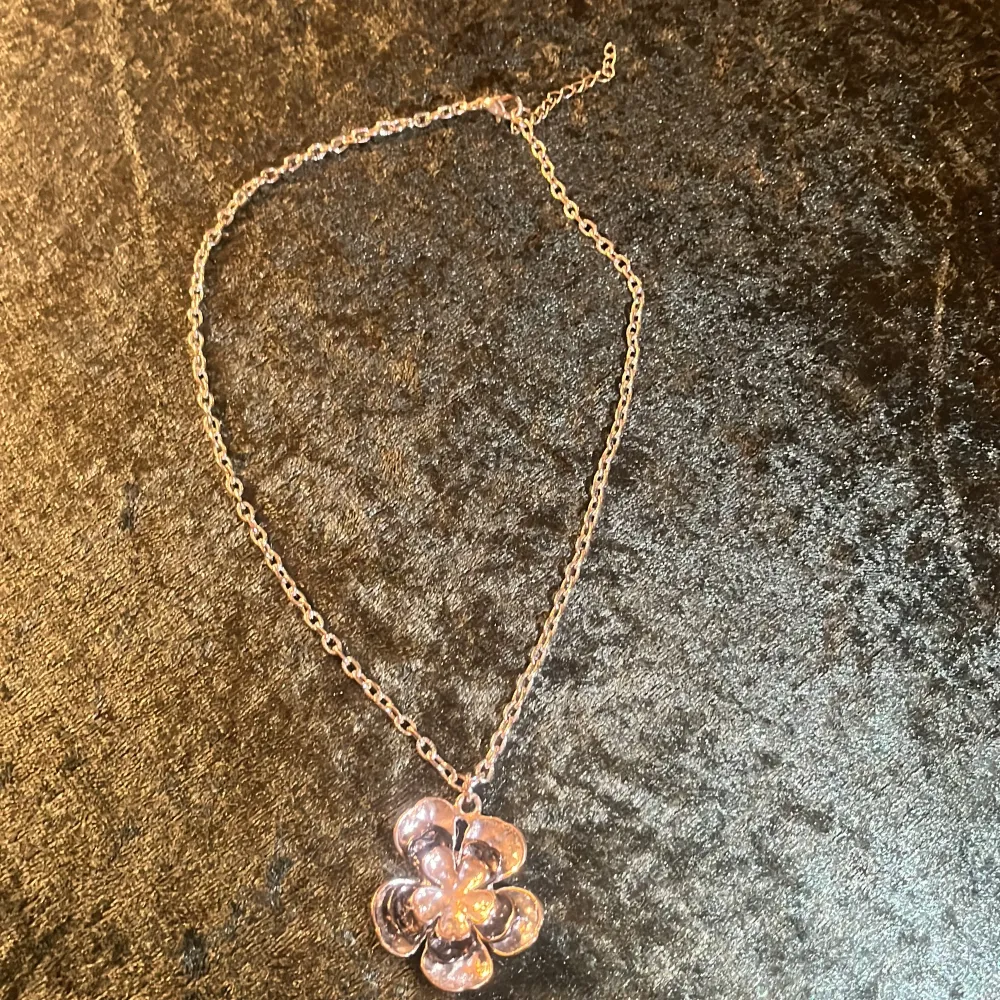 Elegant halsband med en blomformad hängsmycke i guld. Kedjan är tunn och smidig, vilket ger en stilren look. Perfekt för att lägga till en touch av elegans till din outfit.. Asusteet.