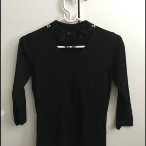 Svart tröja med fransdetalj - Snygg svart tröja med fransdetalj vid halsen. Tröjan har en v-ringad design och trekvartsärmar, perfekt för en stilren look.