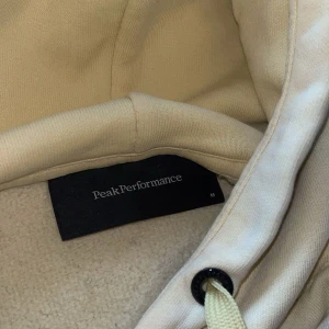 gul/beige hoodie från Peak Performance - Säljer en snygg gul hoodie från Peak Performance med broderad logga på bröstet. 