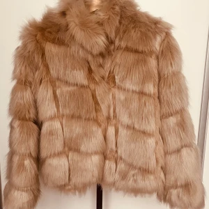 Beige pälsjacka - Säljer en lyxig beige pälsjacka med fluffig textur. Jackan har en elegant design med långa ärmar och en hög krage som ger extra värme. Perfekt för att hålla stilen under kyliga dagar.