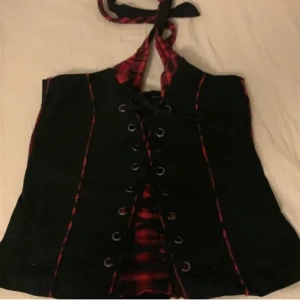 Svart korsett topp - En svart korsett topp, halterneck, med snörning och hint av rutigt mönster, perfekt för dig med mörk alt stil!! Den har som sagt snörning framtill  vilket gör den aningens justerbar. Storleken är L men uppskattar att toppen kanske kan bäras av någon med M också! Mått finns på Slide 3 och 4. Har man fler fundering går det bra att skiva via DM. 🖤 Skickar ej bilder på då plagget inte passar mig. Pris går att förhandla vid snabb affär ❤️