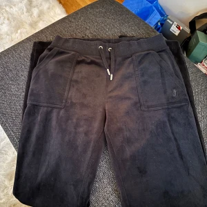 Svarta mjukisbyxor från Juicy Couture - Säljer ett par svarta mjukisbyxor från Juicy Couture. Byxorna har en bekväm passform med snörning i midjan och praktiska fickor både fram och bak. Perfekta för en avslappnad stil. Jättefina, säljer då dom blivit förstora Svarta, ljuset blir inte rättvist.