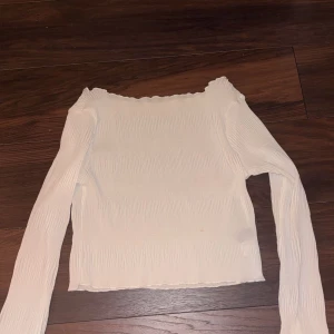 Vit tunn offshoulder topp - Säljer en vit tunn offshoulder topp med långa ärmar. Toppen har en croppad design och har en elastisk ribbad struktur som ger en bekväm passform. Knappt använd.
