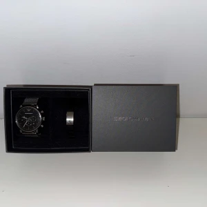 Klocka/armband - Emporio Armani - Snygg svart klocka med silverdetaljer och matchande armband från Emporio Armani. Klockan har en stilren design, Perfekt för den som vill ha en elegant accessoar. Levereras med certifikat och originalförpackning. Använd ett par gånger, nyköpt i Tyskland. Priset kan diskuteras 🤗