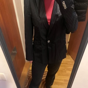 Deep blue randig kostym från J. Lindeberg - Snygg svart kostym från J. Lindeberg med vita ränder. Kavajen (size 38) har knappar och byxorna (size 36) är i matchande stil. Perfekt för en stilren look.