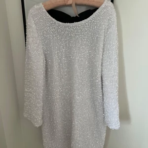 Vit glittrig paljettklänning med svart rosett - Elegant vit klänning med glittrande paljetter och en stor svart rosett på baksidan. Klänningen har långa ärmar och en klassisk passform som passar perfekt för festliga tillfällen, perfekt till jul och nyår. Storlek M men liten i storlek så skulle mer säga att det är en xs/s (Endast testad) Köpt för 450kr