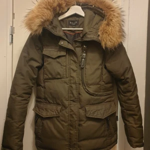 Olivgrön parkajacka med päls från Hollies - Säljer en olivgrön parkajacka från Hollies med en mysig pälsfodrad huva. Jackan har praktiska fickor och stängs med dragkedja. Perfekt för kyliga dagar! Nypris 4500:- pälsen är äkta. Använt den endast vid finare tillfällen. 