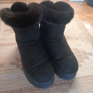 Svarta boots med pälsdetalj - Säljer ett par svarta boots med mjuk pälsdetalj runt skaftet och en dekorativ rosett baktill. Perfekta för kyligare dagar.