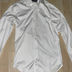 Vit skjorta från Dressmann - Säljer en stilren vit skjorta från Dressmann i slim fit. Skjortan har långa ärmar och knappar framtill. Perfekt för en elegant look.