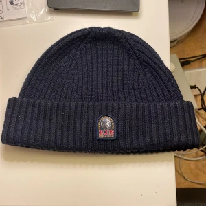 Mörkblå ribbad mössa från Parajumpers - Snygg mörkblå ribbad mössa från Parajumpers med broderad logga framtill. Perfekt för kyliga dagar och ger en stilren look. Passar både till vardags och mer avslappnade tillfällen. Ord pris 899kr