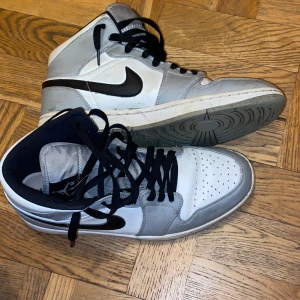 Nike Air Jordans i grått och vitt - Snygga Nike Air Jordans i grått och vitt med svart swoosh. Skorna har hög modell med snörning och perforerad tå för extra ventilation. Perfekta för en stilren look.