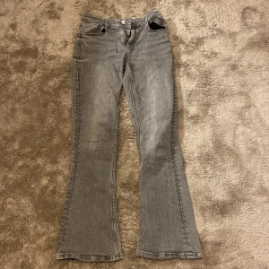 Grå bootcut jeans från Gina Tricot - Snygga grå bootcut jeans från Gina Tricot i storlek 158. De har en klassisk femficksdesign med dragkedja och knapp framtill.