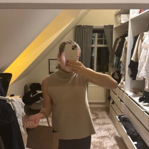 Beige ärmlös polotopp från Zara - Säljer en stilren beige ärmlös polotopp från Zara. Toppen har en hög krage och är perfekt för lager-på-lager eller som den är. Tillverkad i ett mjukt material som ger en bekväm passform.