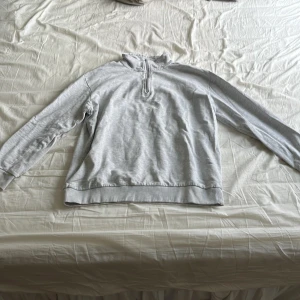 Grå tröja med dragkedja - Säljer en stilren grå tröja med halv dragkedja och långa ärmar. Perfekt för en avslappnad look. Passar bra till både jeans och träningsbyxor.