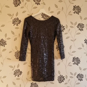 Svart paljettklänning, Divided by H&M, Strl: 38/M, nyår - Snygg svart klänning med paljetter som ger en glittrig look. Klänningen har en djup v-ringning i ryggen och trekvartsärmar. Perfekt för en festlig kväll!