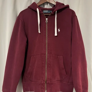 Vinröd hoodie från Polo Ralph Lauren - Snygg vinröd hoodie från Polo Ralph Lauren med dragkedja och huva. Den har en broderad logga på bröstet. Storlek M. Den är i bra skick. Skriv om du har några frågor.
