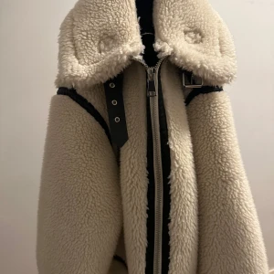 Beige teddyjacka från Zara - Snygg beige teddyjacka från Zara med dragkedja och svarta detaljer. Jackan har en hög krage och långa ärmar, perfekt för kyligare dagar.  Storlek S 