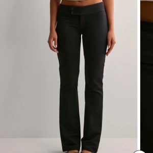 Svarta byxor med låg midja - Snygga svarta byxor med låg midja och bootcut-stil. Perfekta för en stilren look. Byxorna har knappar framtill och är tillverkade i ett bekvämt material. Prislappen är på!